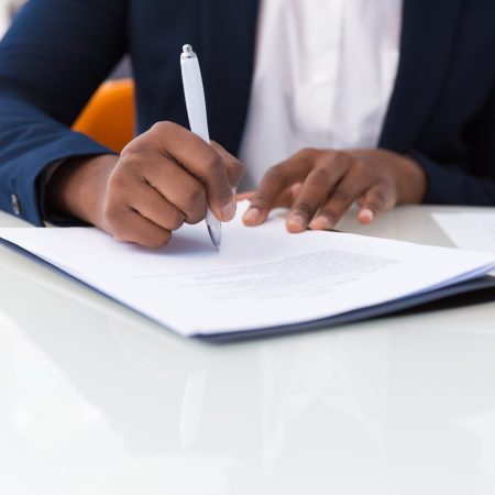 Businesswoman signing contract. African American business woman sitting at table in office, holding pen and writing in document. Legal expertise concept